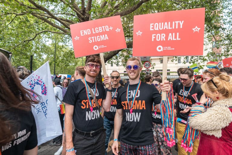 Friends of the Elton John AIDS Foundation at London Pride wearing a black top that says 'End Stigma Now' and two placards that say #End LGBTQ+ Stigma' and 'Equality for all'.