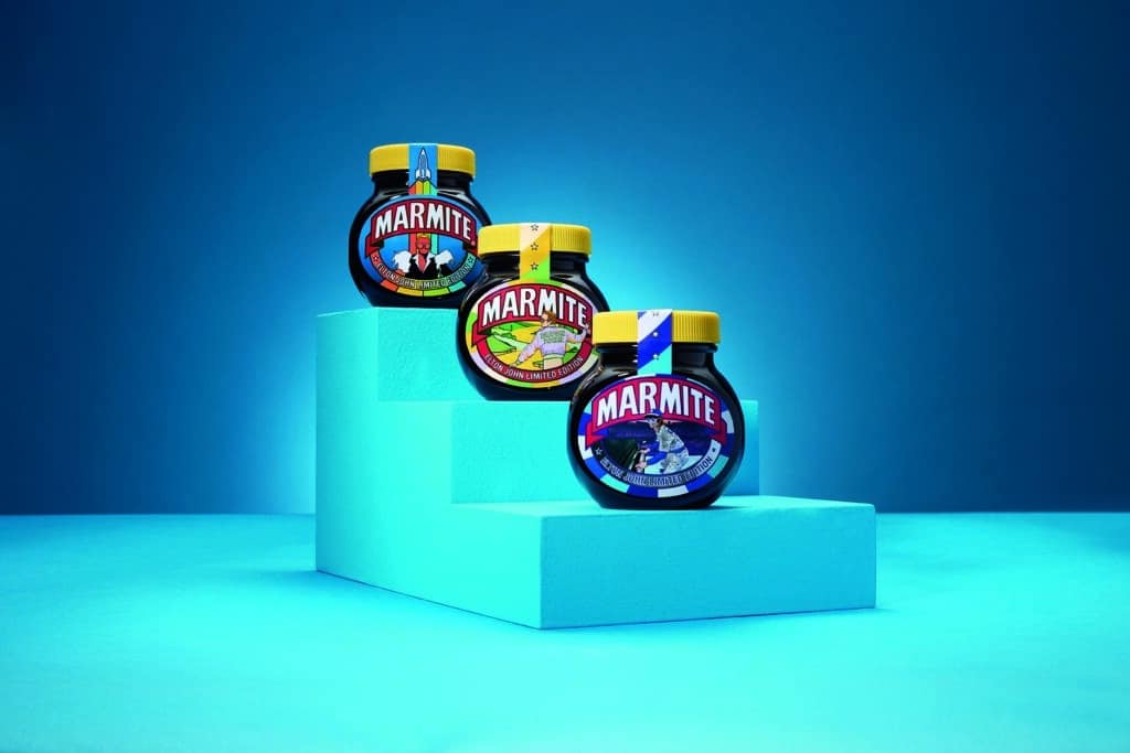 Three limited edition Elton John x Marmite jars sit on blue steps.